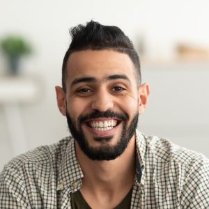 Ana Sayfa 1 portrait of handsome young arab man smiling and looking at camera sitting on sofa at home e1687402178567